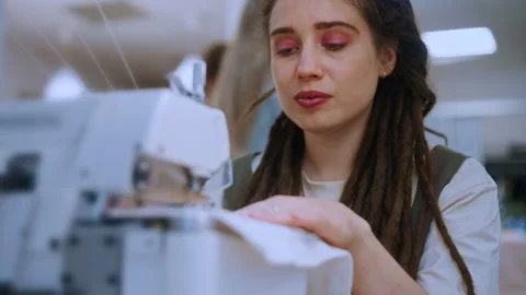 Seamstress with dreadlocks sewing fabric on a machine in a studio Vidéo 335931491