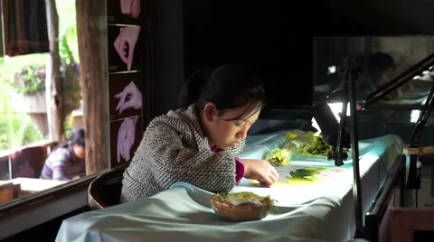 Seamstress is embroiderring patterns on clothes under a lamp in the dark room at Stock Footage 67425334