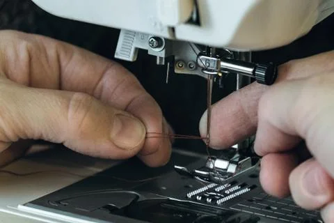 Seamstress inserts the thread through the needle threader of sewing machine Stock Photos