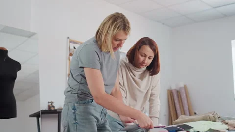 Seamstress mentoring apprentice in fabric selection at creative design studio 스톡 동영상 307135588