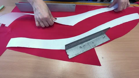 Seamstress positions fabric pattern pieces on red textile for cutting process Vídeos de archivo 346493939