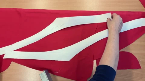 Seamstress positions white fabric pattern on red textile for cutting process Vídeos de archivo 343375603