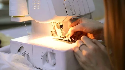 Seamstress quickly inserts a thread with tweezers white overlock Stock Footage 73288930