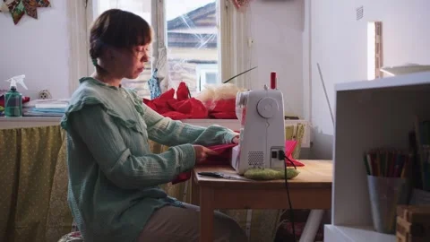 The seamstress sits down at the workplace and begins to sew red clothes Stock Footage 255044172