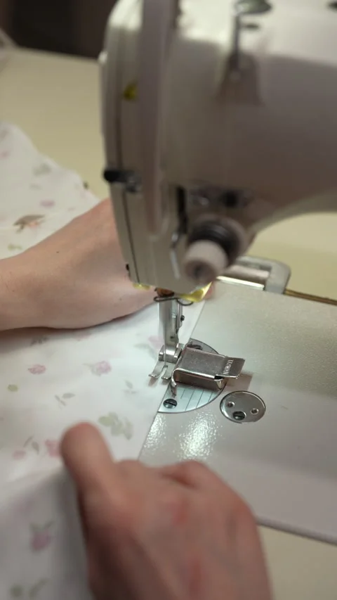Seamstress using sewing machine, focusing on fabric alignment and stitching in Stock Footage 310624704