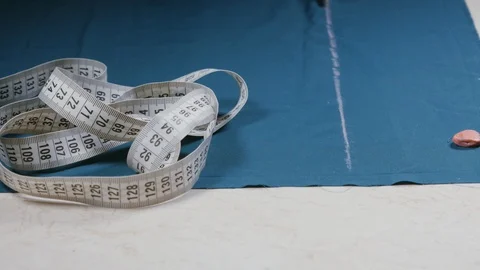 Seamstress when working with scissors cuts a piece of blue fabric on the table Stock Footage 105660371