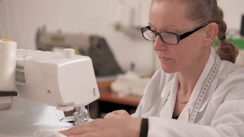 A seamstress working on the sewing machine and stitching pieces of white fabric Stock Footage 100330804