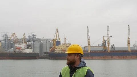 Seaport worker with a beard and a helmet on the background of ships Stock Footage 99352221