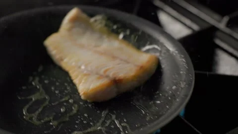 Seared fish fillet cooking in pan with sizzling oil over open flame Stock Footage 313058895