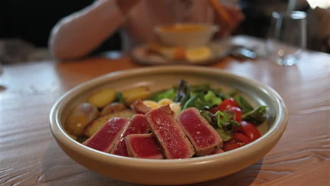 Seared tuna steak slices served with potatoes, fresh salad, tomatoes, and egg on Stock Footage 332623289