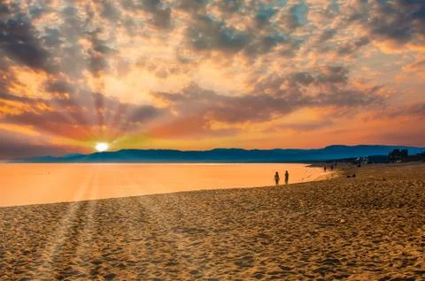Seascape on the beach with dramatic sky and sun lens flare at sunset Stock Photos