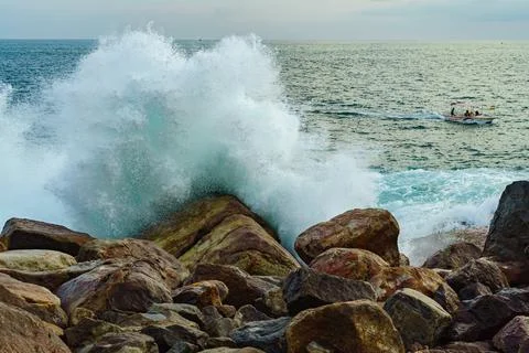 Seascape with big rocks and high waves and a boat Stock Photos
