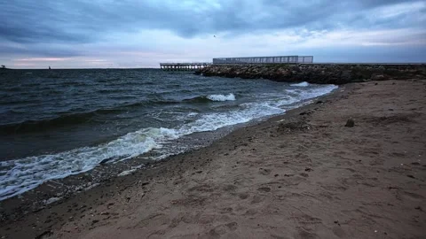 Seascape with wavy ocean and sandy beach during overcast weather with pier in ba Vídeo Stock 346093954