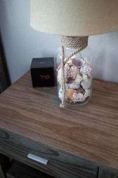 Seashell Filled Lamp on Night Stand Next to Alarm Clock Stock Photos
