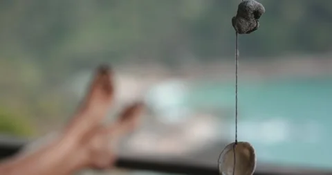 Seashell wind chime hanging gently swaying in tropical breeze with tourist Stock Footage 281087899