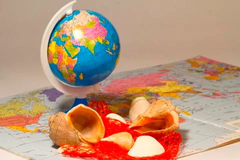 Seashells and small globe on a book with a geographical map. Stock Photos