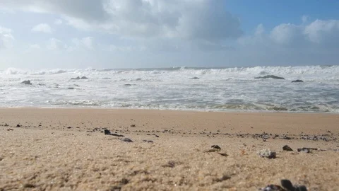 Seashells on sandy beach with rough, turbulent white waves on ocean. Slow motion Stock Footage 119292958