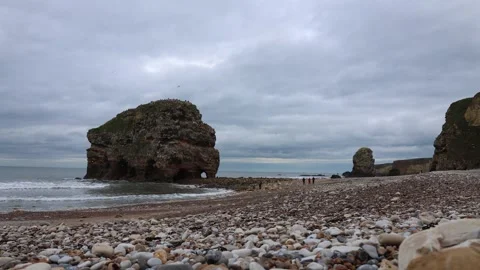 Seashore on a Cloudy Day With Rocks and a Group of People in the Distance Stock Footage 246942867