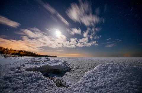 Seashore covered with ice under a starry sky with moon. Stock Photos