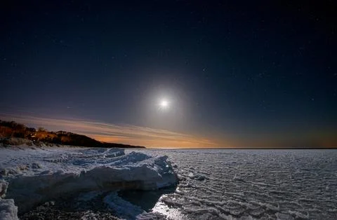 Seashore covered with ice under a starry sky with moon. Stock Photos