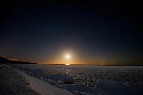 Seashore covered with ice under a starry sky with moonset. Stock Photos