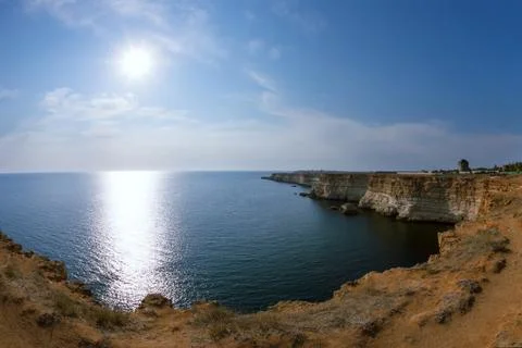 Seashore with high cliffs, under a blue sky with clouds and sun Stock Photos
