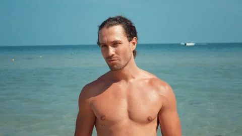 On seashore self-confident handsome man who puts on sunglasses. Man exudes Stock Footage 275083073