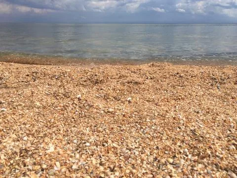 Seashore from small seashells blue sky and white clouds Stock Photos