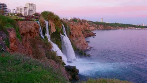 Seaside cityscape scene. Urban cliffs meet cascading waterfalls at sunset 스톡 동영상 331556895