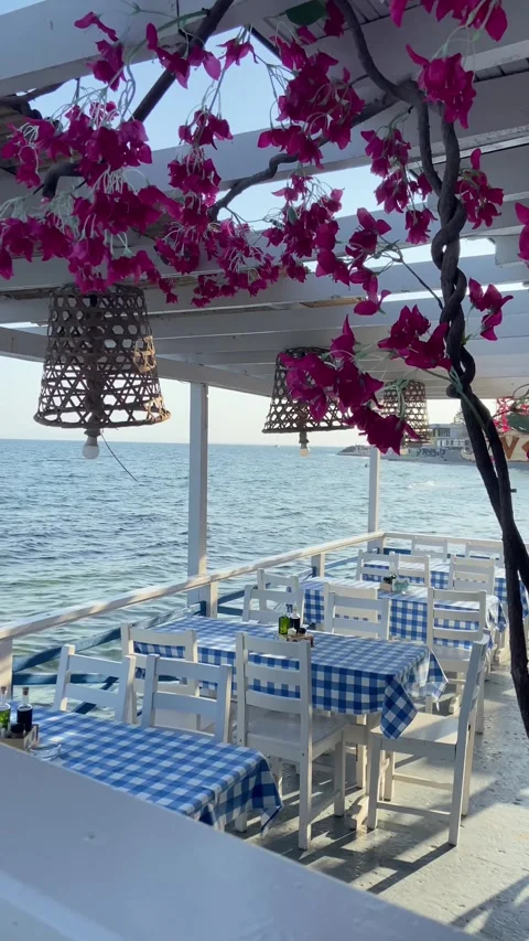 A seaside dining area with blue and white checkered tablecloths, white chairs, a Stock Footage 293090124