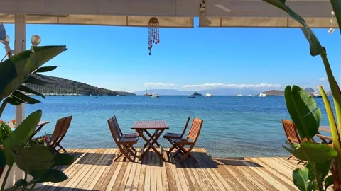 Seaside dining deck with wooden tables and chairs overlooking a beautiful Stock Footage 318345487