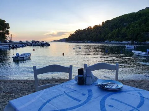 Seaside Dinner Table at Sunset Over Calm Harbor With Boats and Coastal Hillside Photos