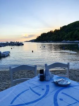 Seaside Dinner Table at Sunset Over Calm Harbor With Boats and Coastal Hillside 스톡 사진