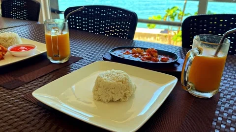 Seaside restaurant table with rice plates, seafood dishes, and fresh juice, set Stock Footage 333890209