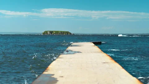 A seaside scene featuring a pier, blue water, and a jet ski cutting through.. Stock-Footage 345626331