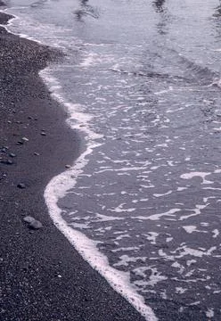 A seaside scene with waves rolling onto the beach shore with sand and pebbles. Stock Photos