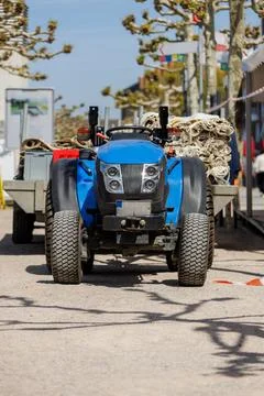 Seaside Setting Featuring Blue Tractor Pulling Utility Carts Past Shops Stockfoto's