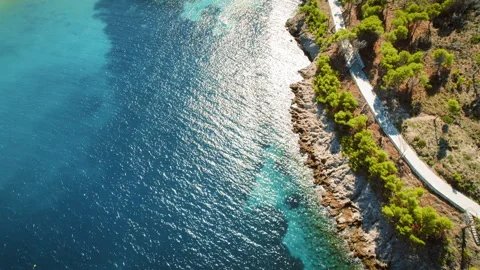 Seaside trail winding through forested area next to beachside village and cliffs Stock Footage 345687577