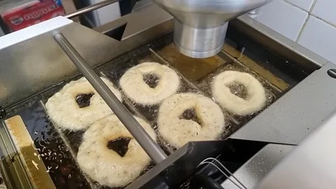Seaside vendor automated machine cooking raw donut batter rings frying in oil Stock Footage 308350063