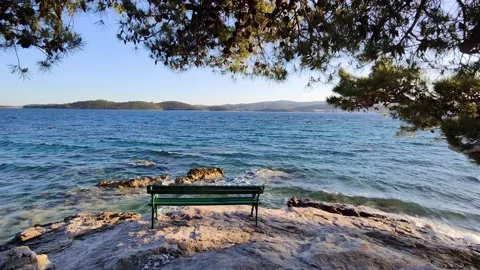Seaside view during sunset with a bench on the rock overlooking the waves Stock Footage 221582546