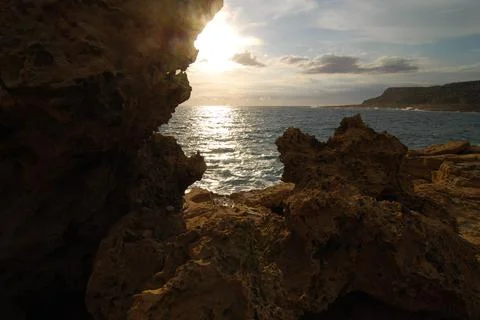 Seaside view where the sunrays pierce through a gap between coastal rocks Stock Photos