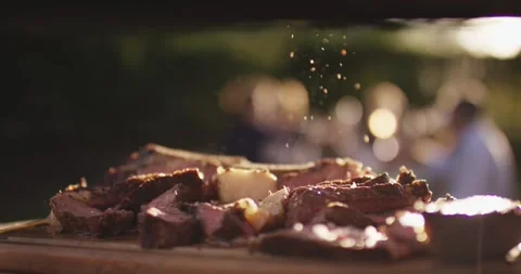 Seasoning falling in warm evening light onto freshly sliced grilled steak on a Stock Footage 339977936