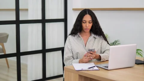 Seated at computer desk at home mid adult woman looks at her phone in shock Stock Footage 276998185