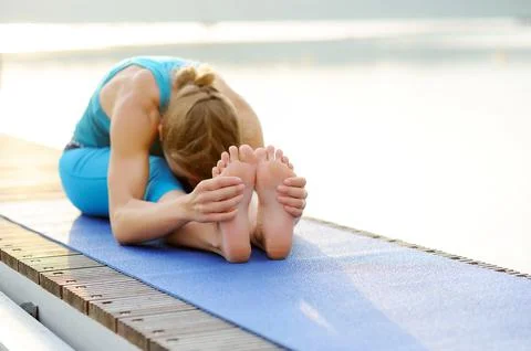 Seated Forward Bend yoga position practiced by yoga girl at the river bank Stock Photos