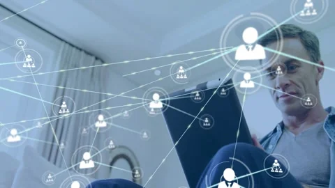 Seated man angling tablet at home, initiating tech node overlay forming over Stock Footage 330208269
