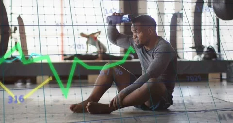 Seated man postset dousing head with bottle while cooling as fitness graphs Stock Footage 323372919