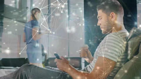 Seated man scrolling phone sipping cup in office causing network overlay while Stock Footage 334013893