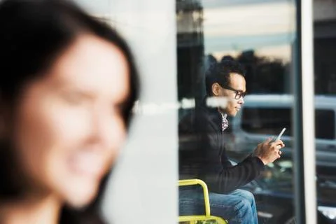 A seated man seen through a window looking at a cellphone, with an out-of-focus Stock Photos