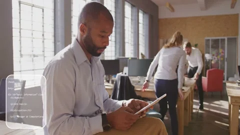 Seated man tapping tablet, generating UI code overlays and guiding team tech Stock Footage 333351238