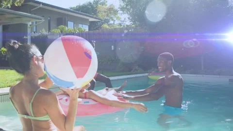 Seated man tossing beach ball, woman in pink pool float reaching, friends Stock Footage 333018557